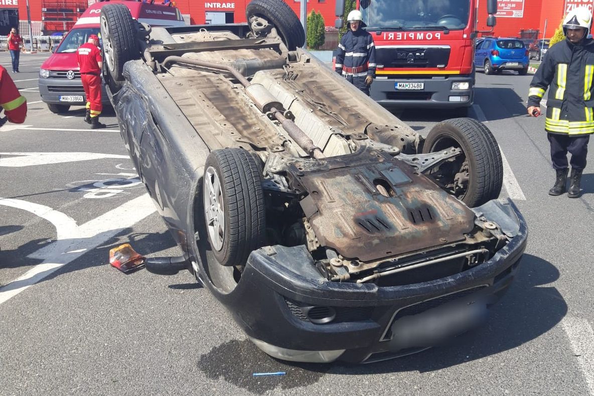 Accident incredibil în parcarea unui supermarket. O mașină, răsturnată