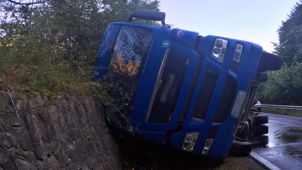 FOTO | TIR plin cu bușteni, răsturnat într-o curbă periculoasă, în Bistrița-Năsăud